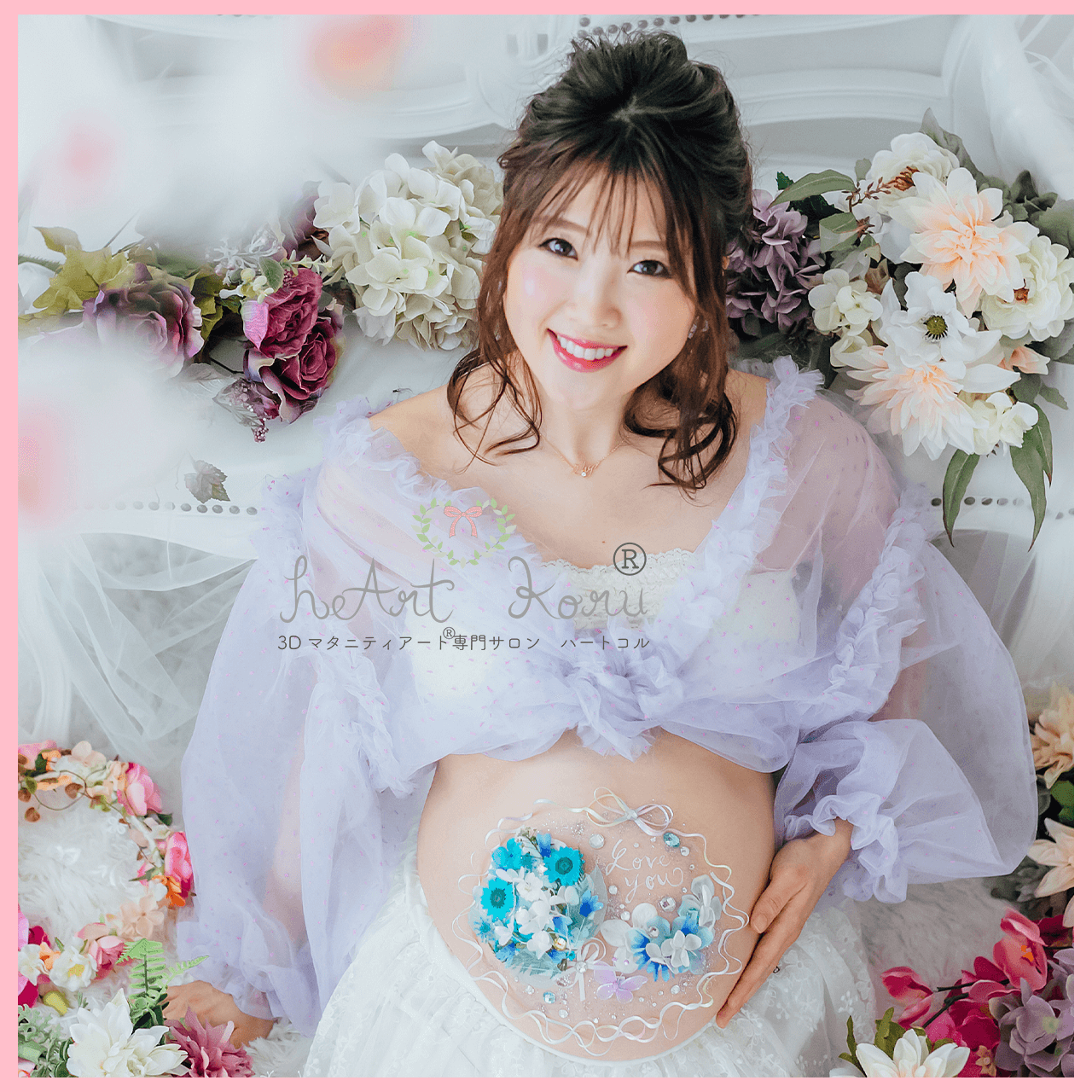 妊婦さんがお花に囲まれて座った撮影です。お腹には瑠璃色の鮮やかな3Dマタニティペイントが施されている。