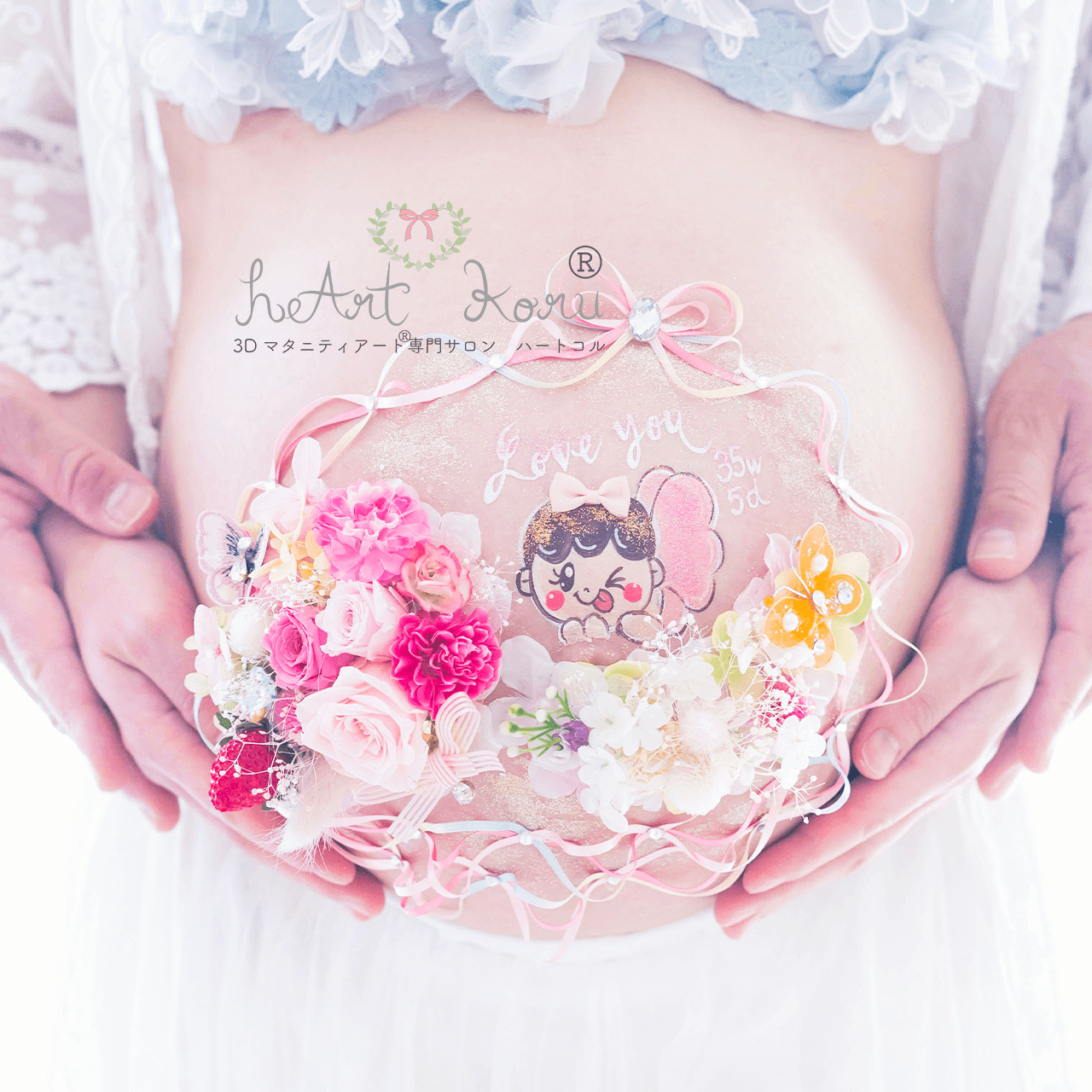 妊婦さんのまあるいお腹に、立体の3Dマタニティペイントが施されている。真ん中に赤ちゃんのイラストがあり、そこを囲むようにピンクやカラフルなお花たちが包み込んだマタニティペイントのデザイン。