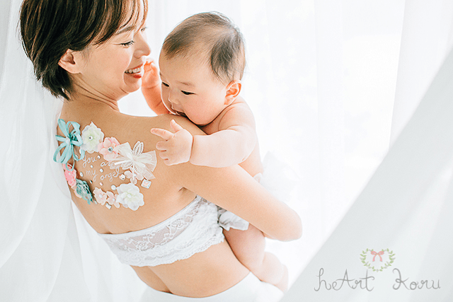 水色のリボンをベースに、白、ピンクの鮮やかなお花を添えた授乳ペイント。赤ちゃんを抱きかかえるシーンを撮影した心温まる授乳フォトです。