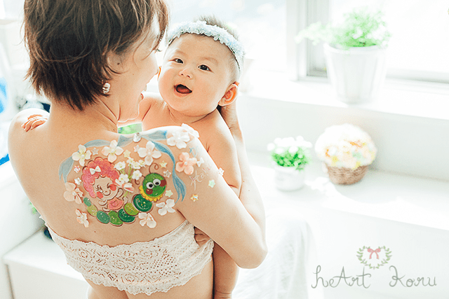印象的なキャラクターが2種類描かれた授乳ペイント。可愛いキャラクターと肩まではみ出したお花が可愛いデザインです。赤ちゃんを抱き上げたシーンを撮影した授乳フォトです。