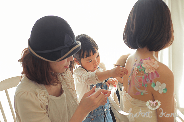 背中にコウノトリが描かれた授乳ペイント。お子さんがデコパーツを貼るところを撮影した一枚です。