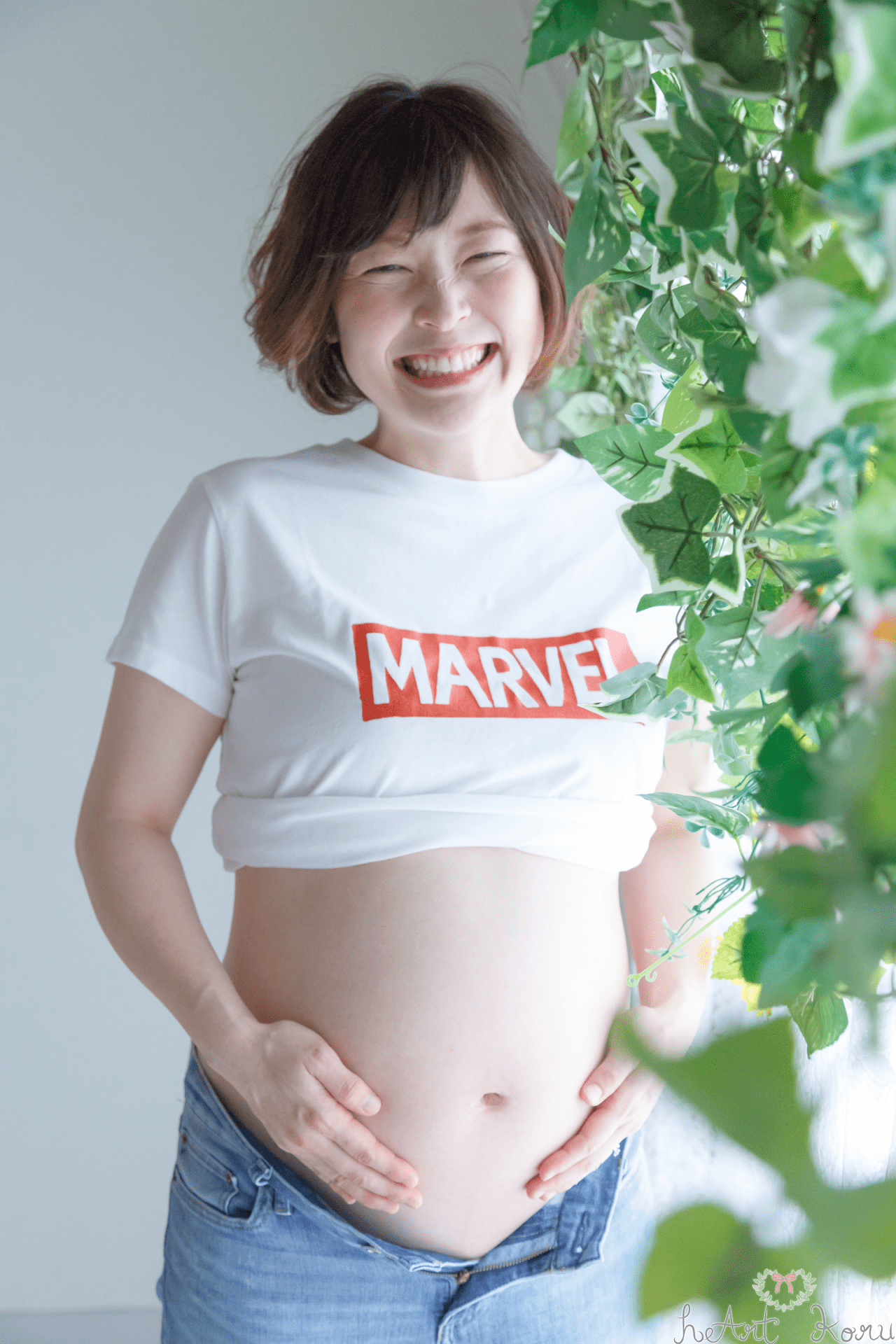 マタニティフォト（ペイント前）。妊婦さんがデニムとTシャツをマタニティフォトの衣装として着ている可愛いマタニティ撮影。妊婦さんが笑顔で写っている。自然光と緑が綺麗なマタニティ写真。