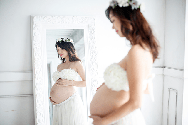 美しい自然光で撮影したマタニティフォト。ホワイトのマタニティフォト衣装と おしゃれなお花の冠がかわいい。鏡に映った、妊娠しているありのままの姿が神秘的なマタニティ写真（撮影）。2人目妊娠中。