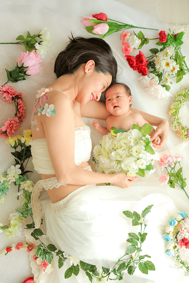 授乳フォト、ベビーフォト、親子フォト。授乳ペイントのコースのデザイン。お母さんと赤ちゃんが一緒に横になって戯れている可愛い親子写真。周りには、お花などが散りばめられている。綺麗な自然光がおしゃれな写真。