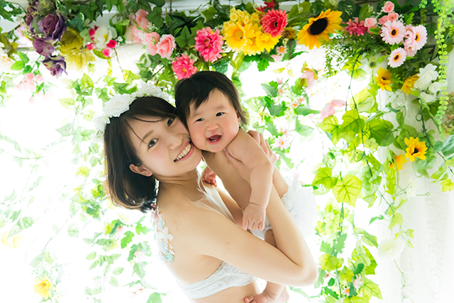 授乳フォト、ベビーフォト、親子フォト。授乳ペイントのコースのデザイン。お母さんが赤ちゃんだきあげている可愛い親子写真。綺麗な自然光と緑がおしゃれな写真。